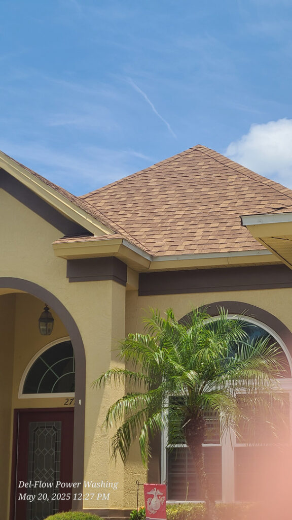 del-flow power washing cleaning a roof with shingle tiles and maintaining the home's exterior in bright daylight