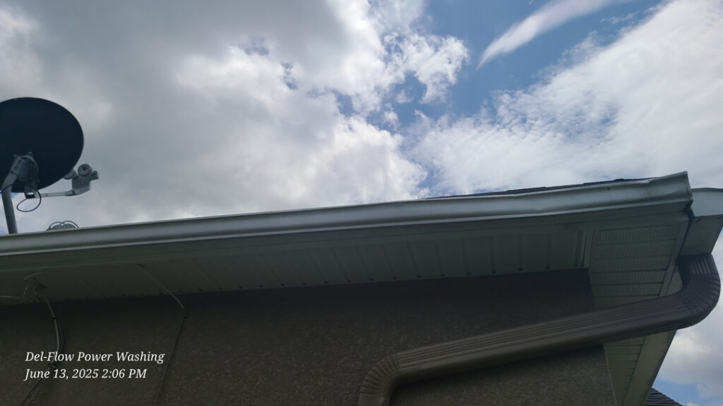 del-flow power washing cleaning a roof edge and gutters with cloudy skies in the background