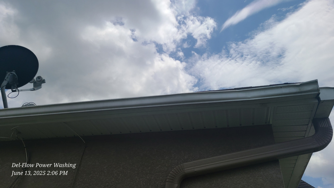 del-flow power washing cleaning a roof edge and gutters with cloudy skies in the background