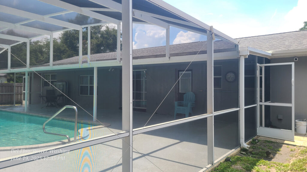 del-flow power washing cleaning a screened pool enclosure and surrounding area with clear blue water in the pool