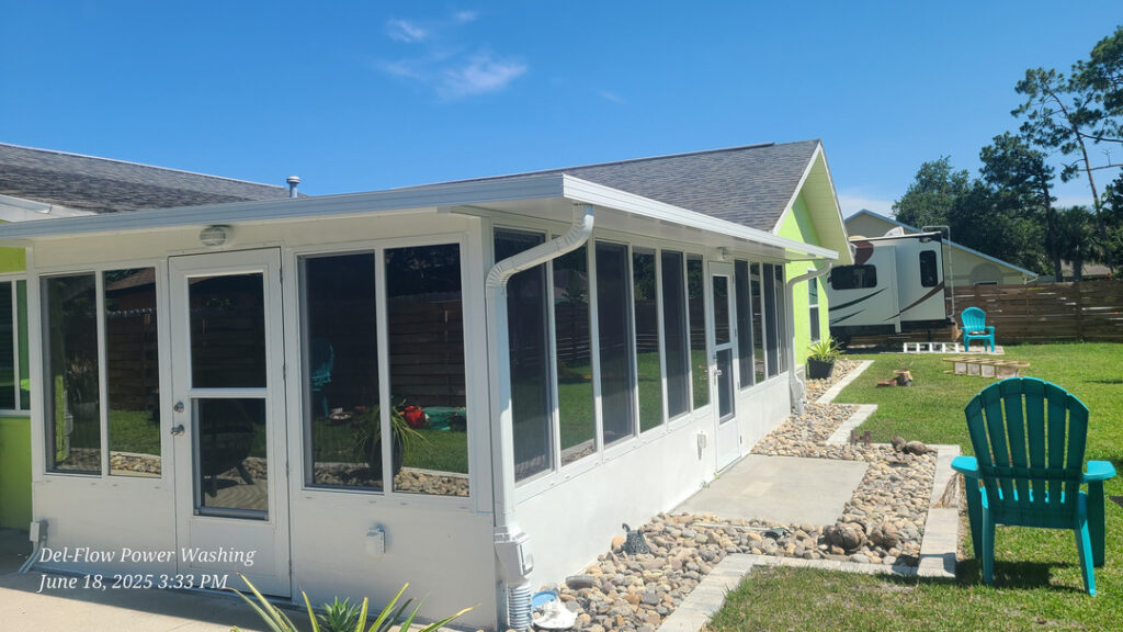 del-flow power washing cleaning a sunroom with large glass windows in a well-maintained yard