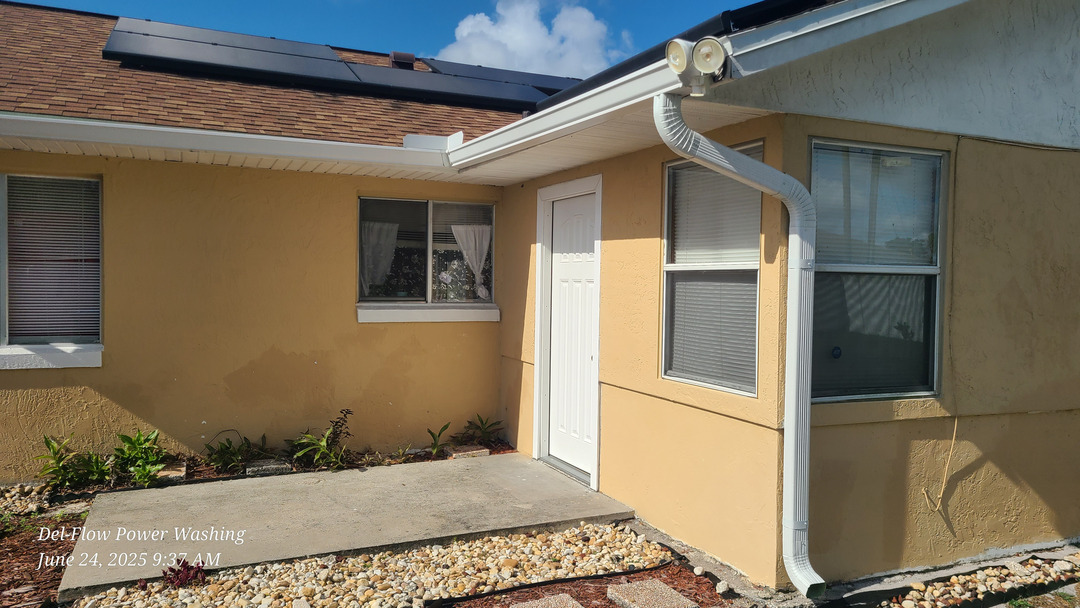 del-flow power washing cleaning a tan stucco exterior and concrete walkway with visible landscaping around the entrance